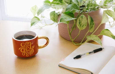 black retractable pen on notebook with a coffee mug nearby