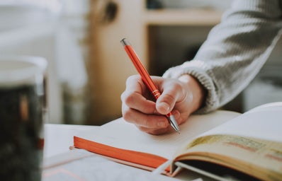 Person holding a red pen while writing in a notebook.