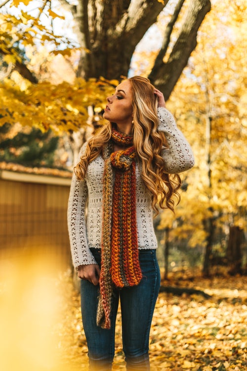 woman outside wearing sweater and scarf, surrounded by fall trees