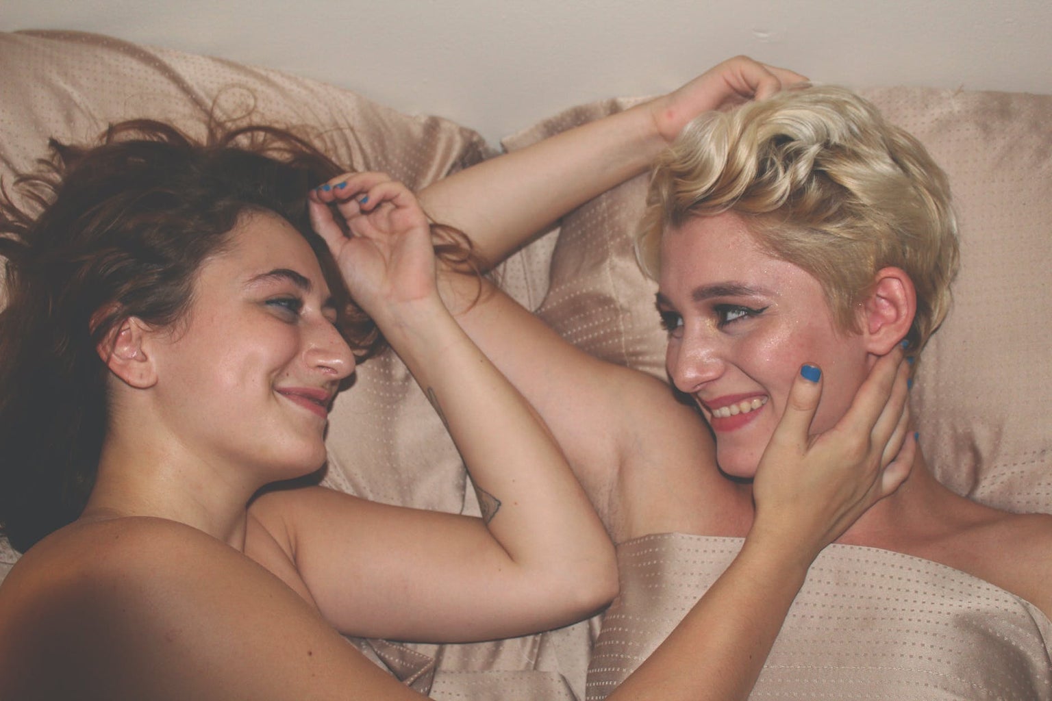 two women smiling at each other while laying in a bed