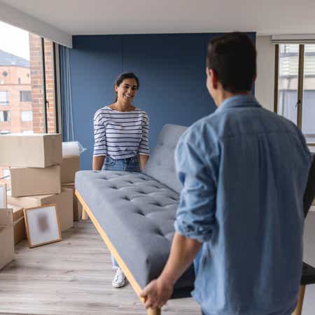 Smiling couple carrying a couch into their apartment