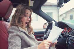 Young girl sitting inside of a car and reading fine papers, looking frustrated