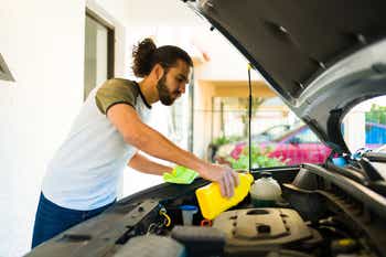 Young man changing the oil of his car while checking the engine
