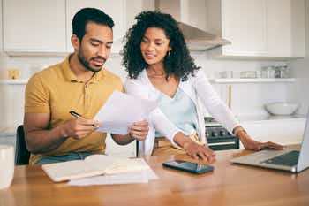 Couple, insurance paperwork and budget planning with laptop, bills and finance with taxes and mortgage.