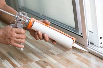 Men’s hand uses silicone adhesive with a glue gun to repair worn windows