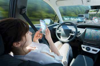 Young woman using a smart phone behind the wheel in a self-driving car