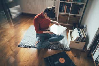 Young woman sitting on floor and listening to her vinyl records collection