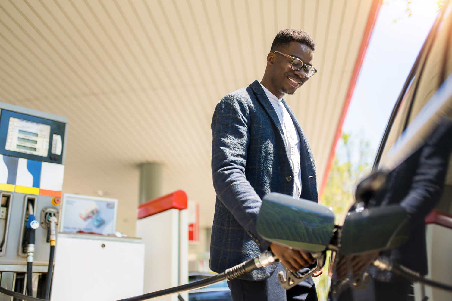Young African American businessman sipping fuel into his car tank at the gas station.