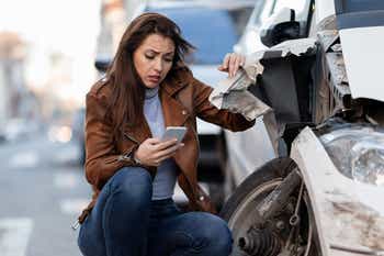 Young sad woman text messaging on smart for after a car crash on the road.
