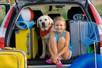 Little girl and dog sitting in the back of a packed up car
