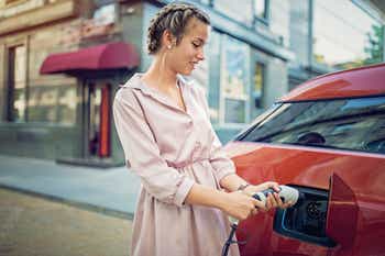 Young woman charging her electric car in the city