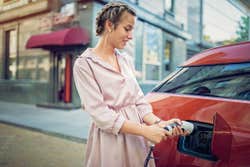 Young woman charging her electric car in the city