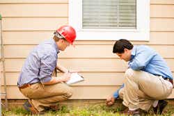 Repairmen, building inspectors, exterminators, engineers, insurance adjusters, or other blue collar workers examine a building/home's exterior wall and foundation.