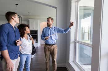 Male Real Estate Agent shows couple a view through living room windows in the home.