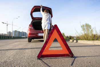 Woman opening trunk and placing hazard sign by car