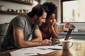 Young couple using a laptop while doing their budget paperwork in their kitchen at home