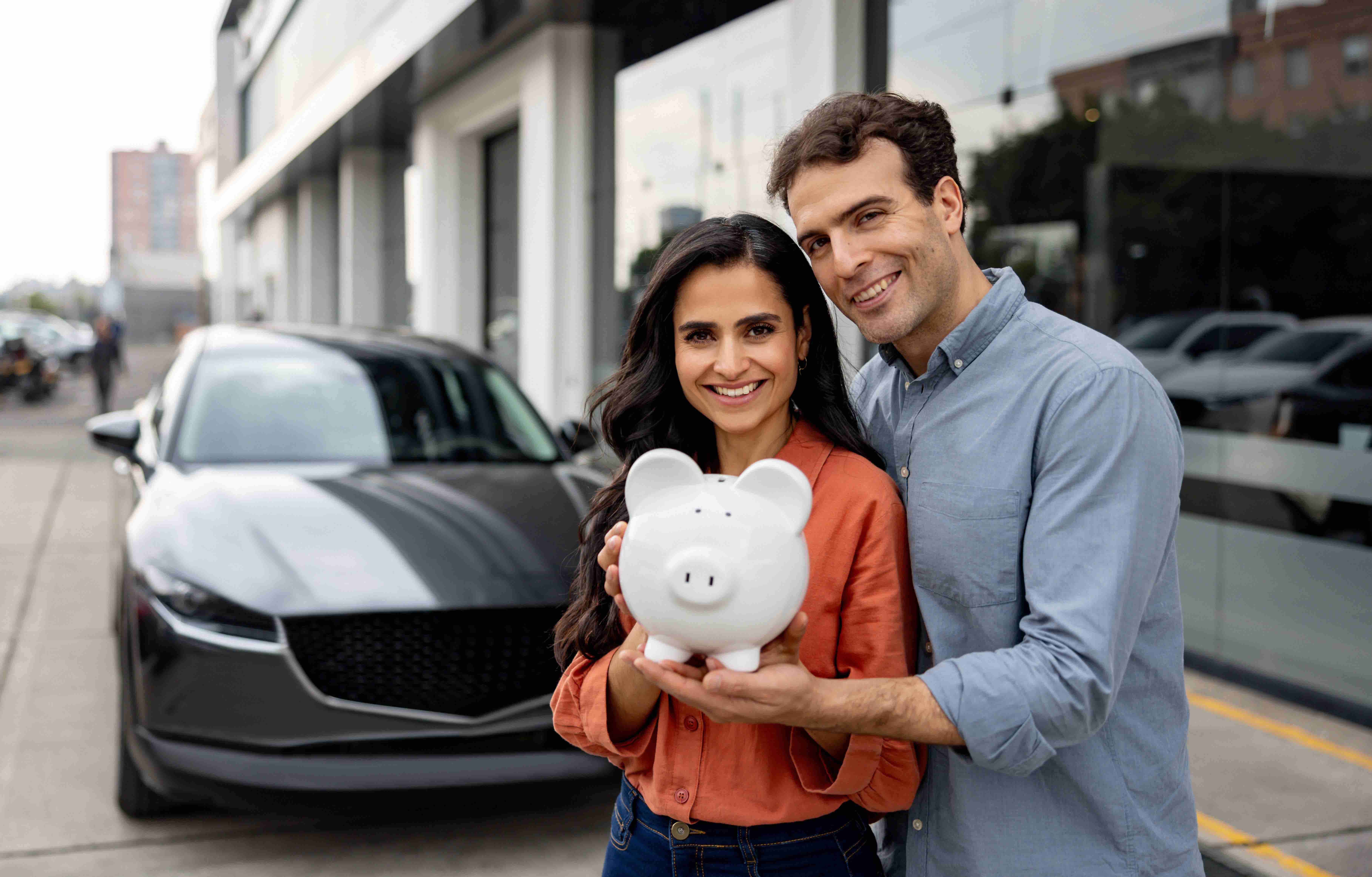 Portrait of a happy couple holding a piggy bank after buying auto insurance in front of their car.