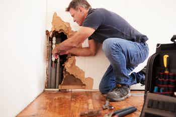 Middle aged man repairing burst water pipe