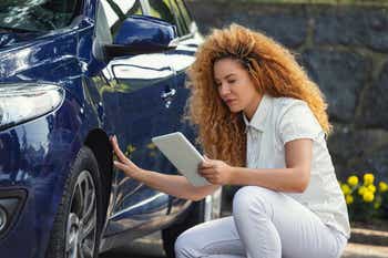 Woman automobile insurance adjuster inspecting damage to vehicle