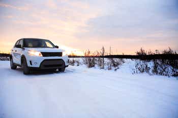 White SUV driving in the snow at sunset