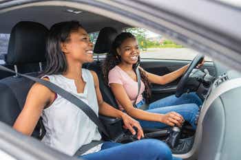 A young black teenage driver seated in her new car with her mother