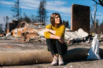 Woman sitting at front of burned down house