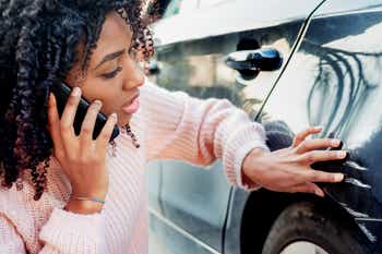 Woman on phone inspecting car damage