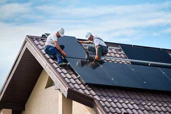 Workers building solar panel system on rooftop of house