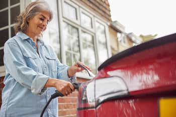 Mature woman attaching charging cable into electric car at home