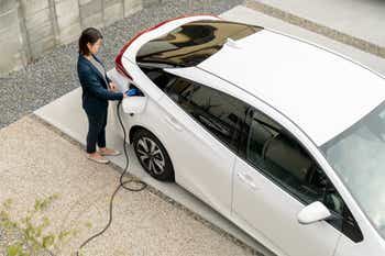 Woman charging her electric vehicle in driveway of home