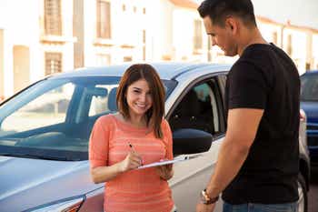 Happy young woman shopping for insurance with an agent beside her car