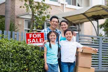 Family standing near for sale sign in front of house