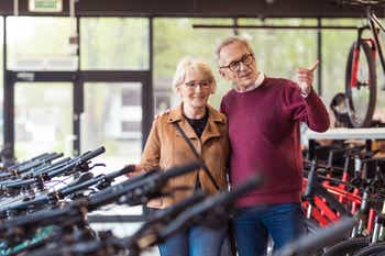 Senior woman and senior man watching bicycles in bike shop. Man pointing with index finger.