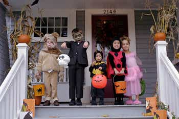 Five children wearing Halloween costumes, standing on a porch and making funny faces