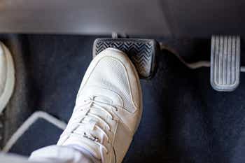 Pair of white sneakers on the floor in a car pressing brake against gas, carefully driving car concept
