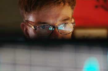 A mature man studying a colourful computer display which is reflected in his glasses.