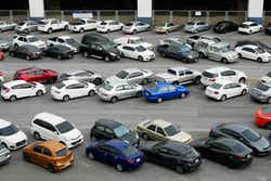 Cars parked in outdoor parking lot at with many of buildings in background.