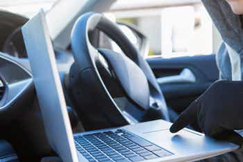 Burglar using a laptop to hack into a vehicle