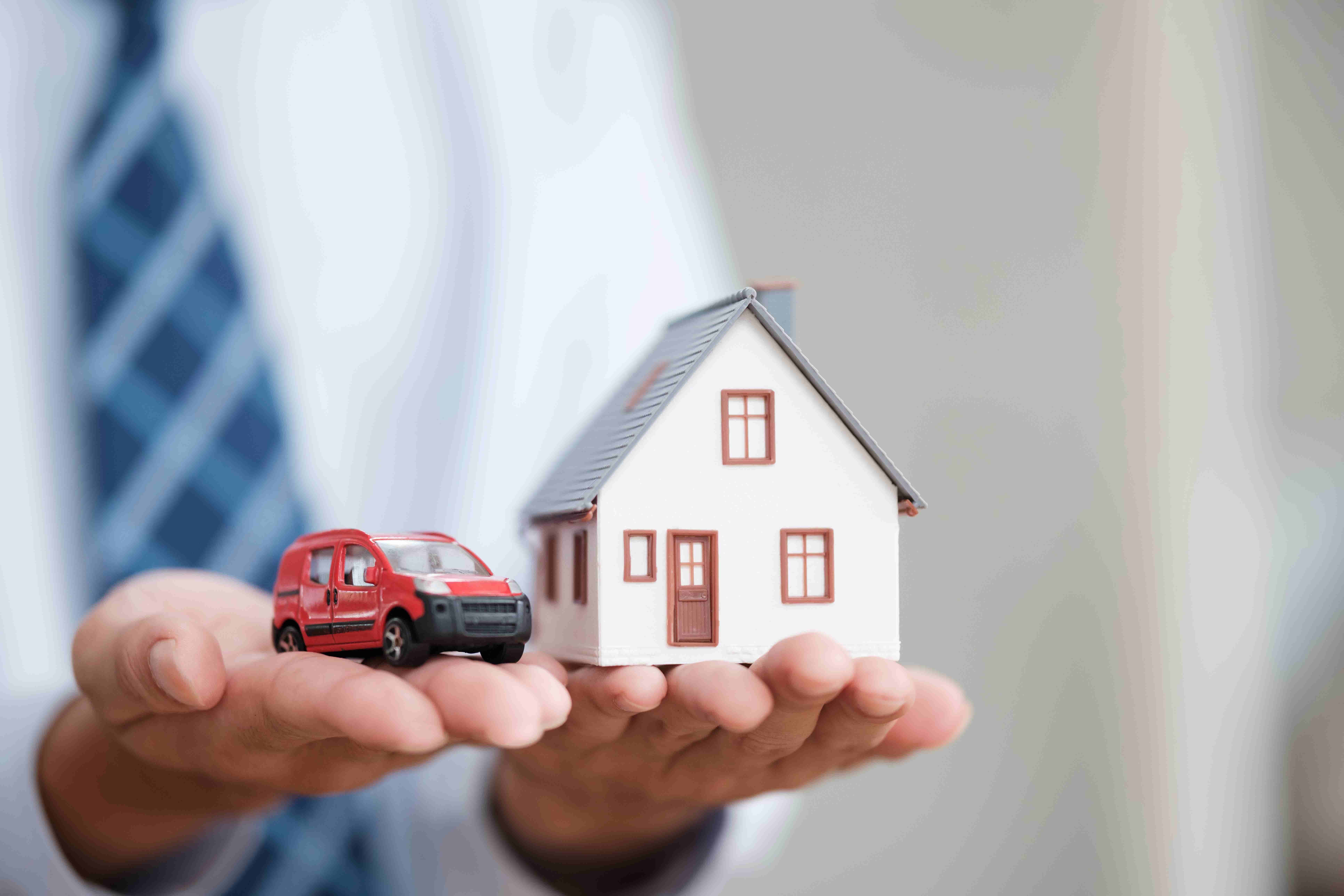 Hands holding a car and a house, symbolizing bundled home and auto insurance.