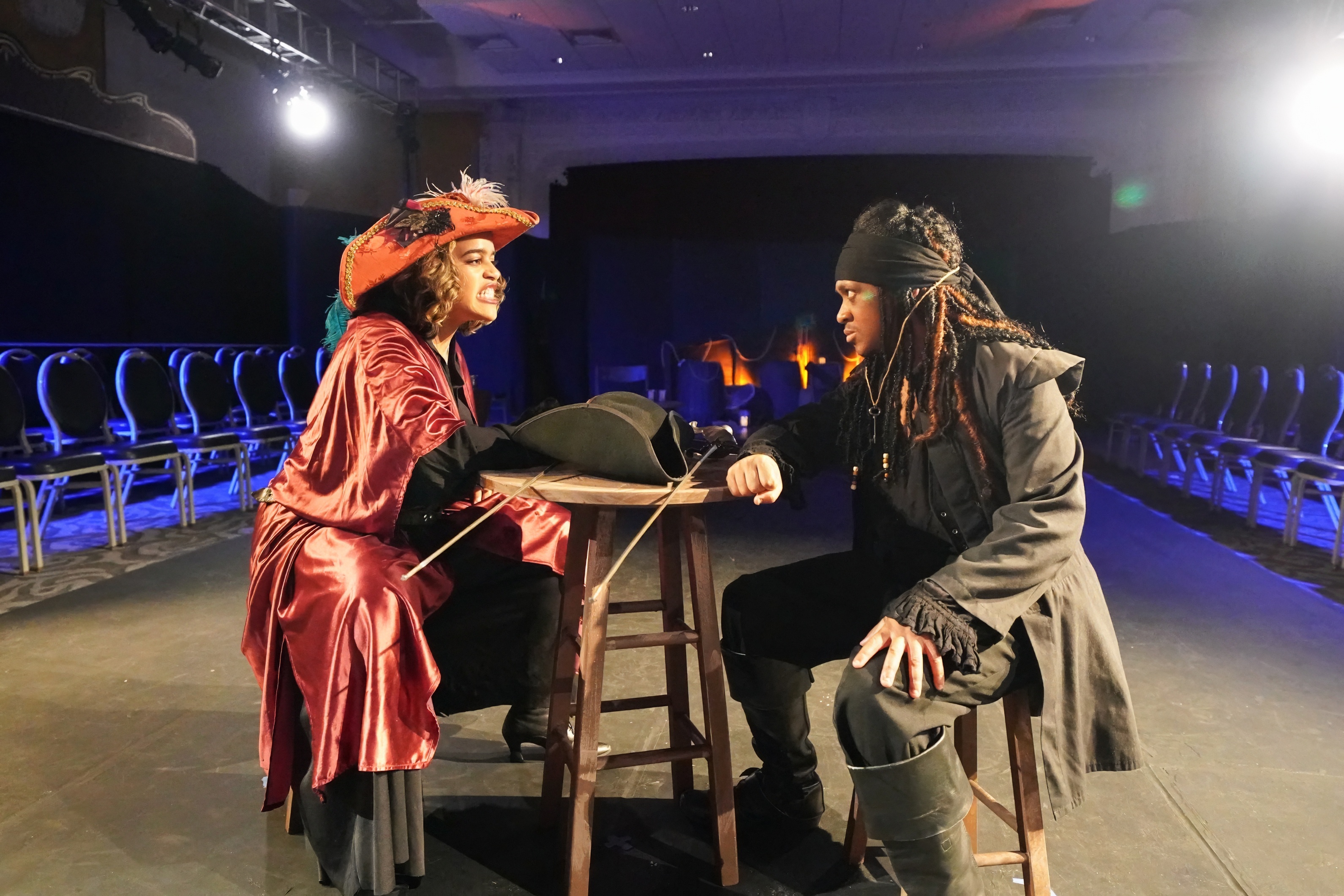 Two student actors dressed as pirates face each other at a table 