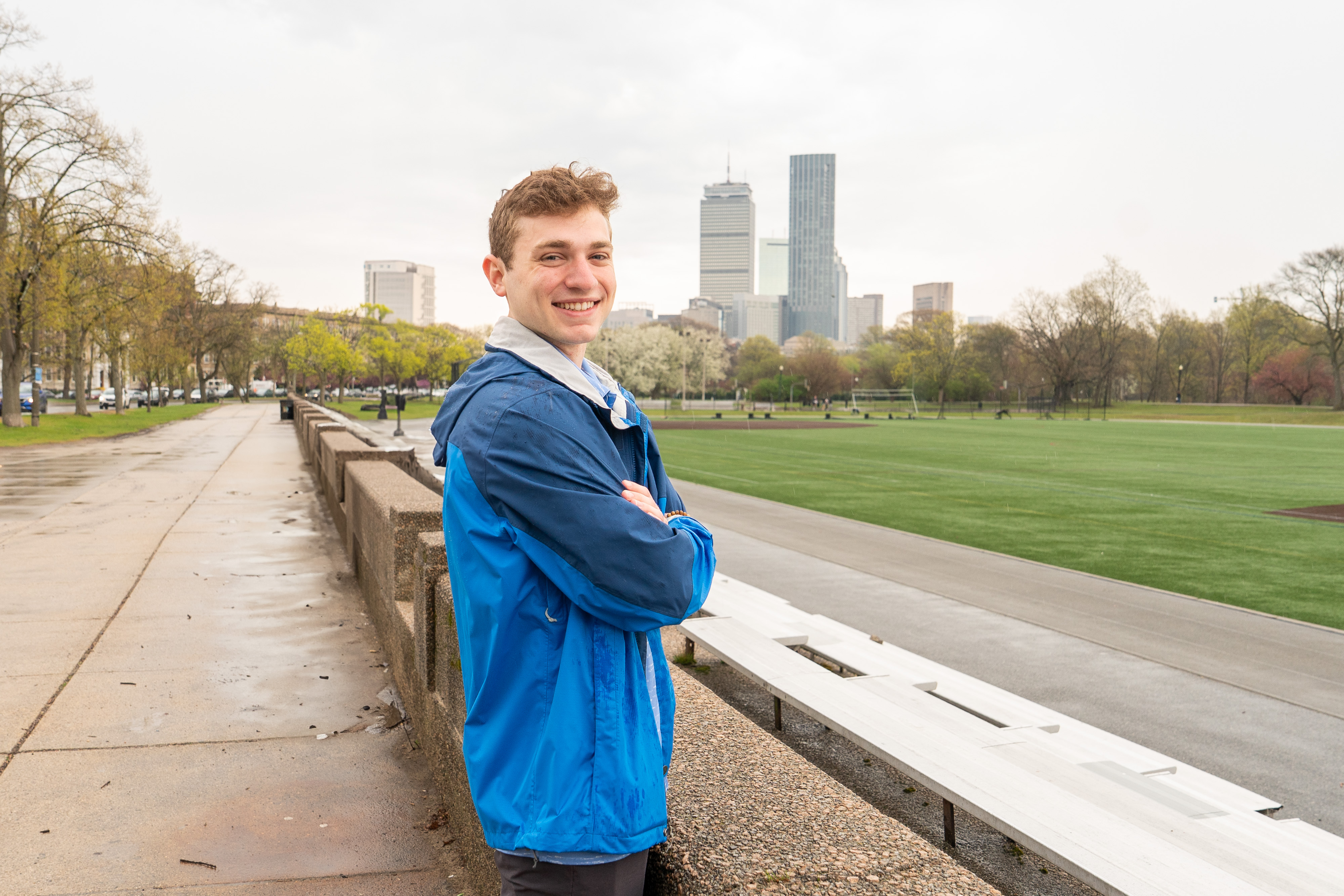 A man in a blue jacket in front of the Boston skyline 