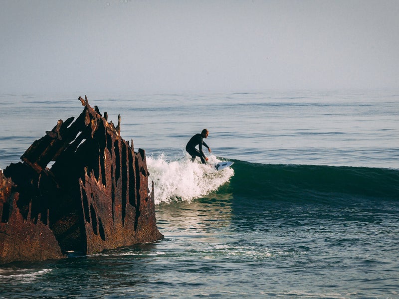 Person surfing near a rusted shipwreck