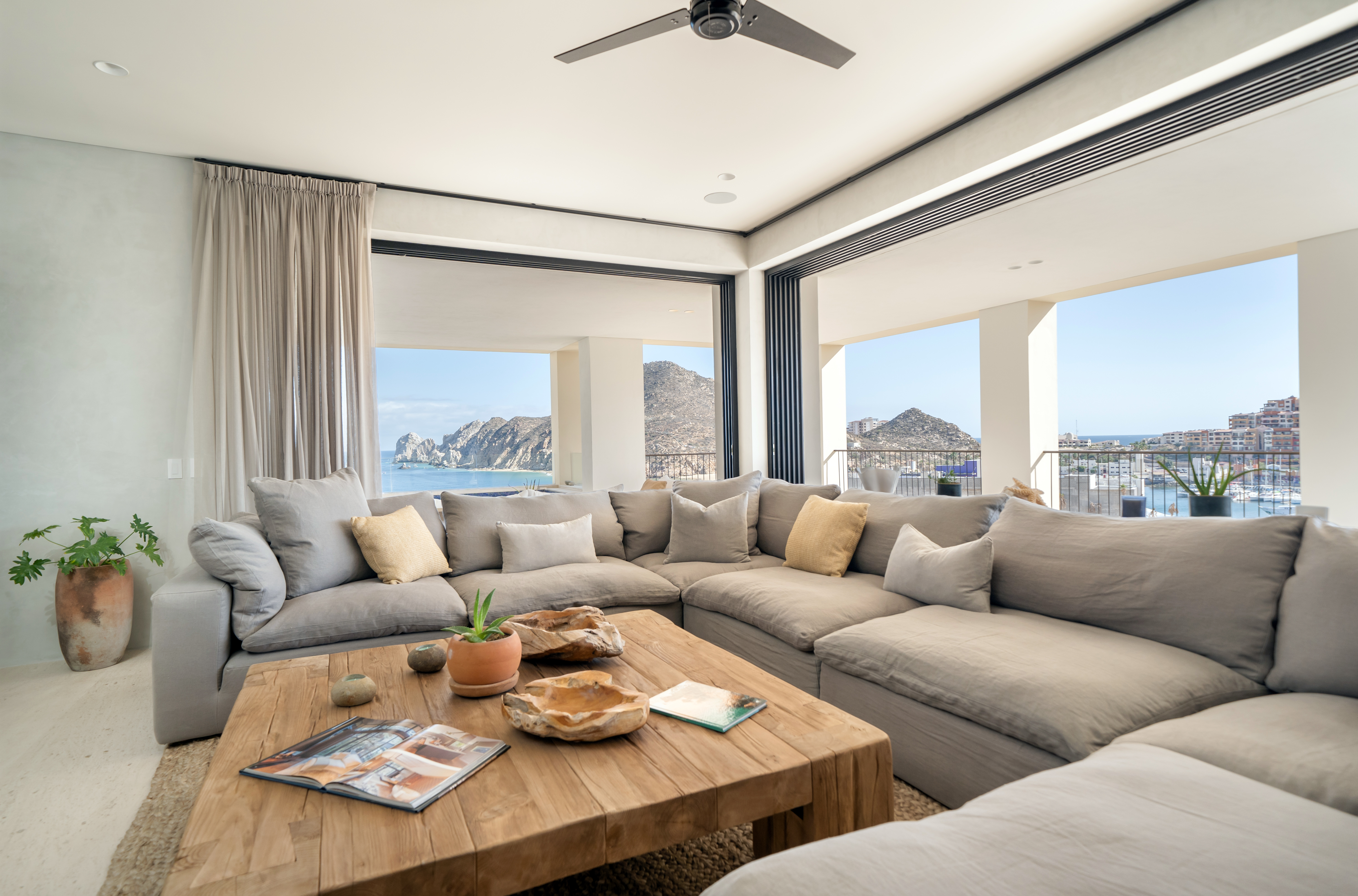 Windows with a panoramic view of the seascape outside line a large room with a wrap around sectional