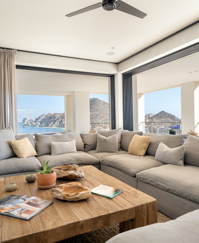 Windows with a panoramic view of the seascape outside line a large room with a wrap around sectional