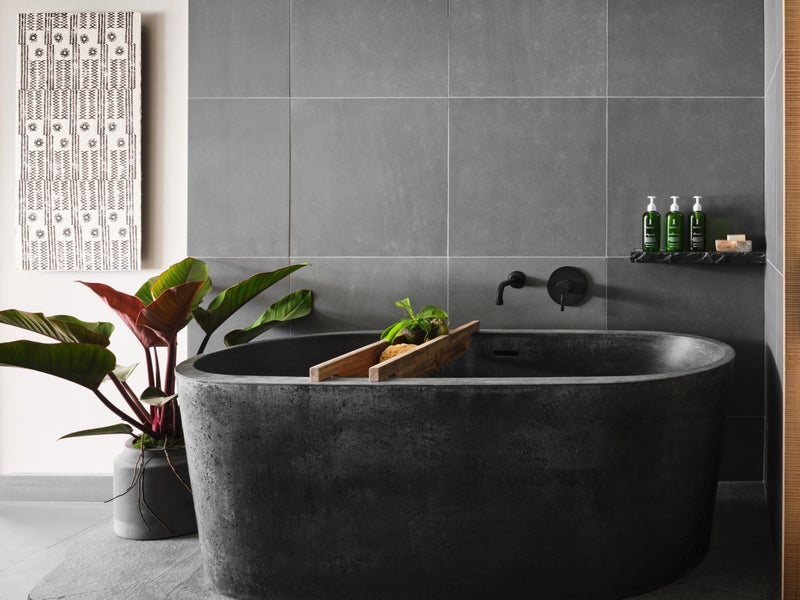 A large granite bathtub sits atop another slate of granite with a gray tile backdrop