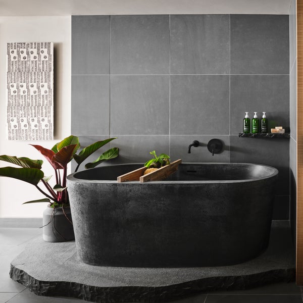 A large granite bathtub sits atop another slate of granite with a gray tile backdrop