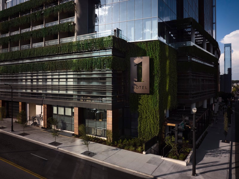 Outside of hotel made of glass, green foliage and large 1 Hotels logo