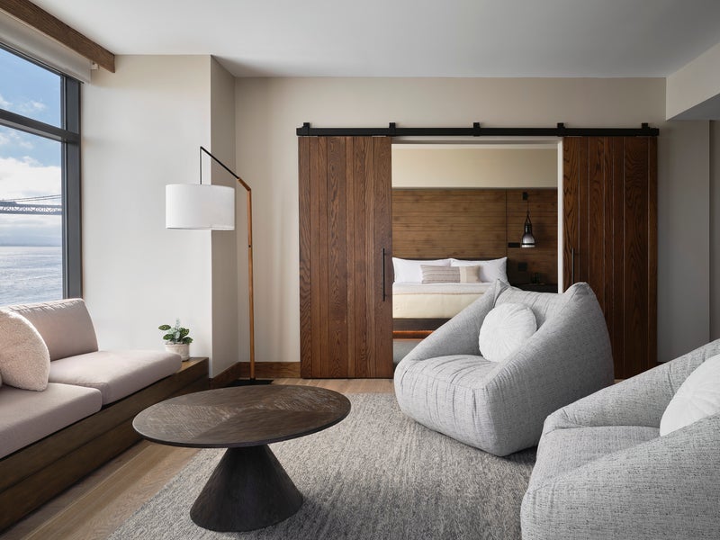 Two large gray chairs and a sofa positioned around a dark brown circular coffee table, overlooking views of the water