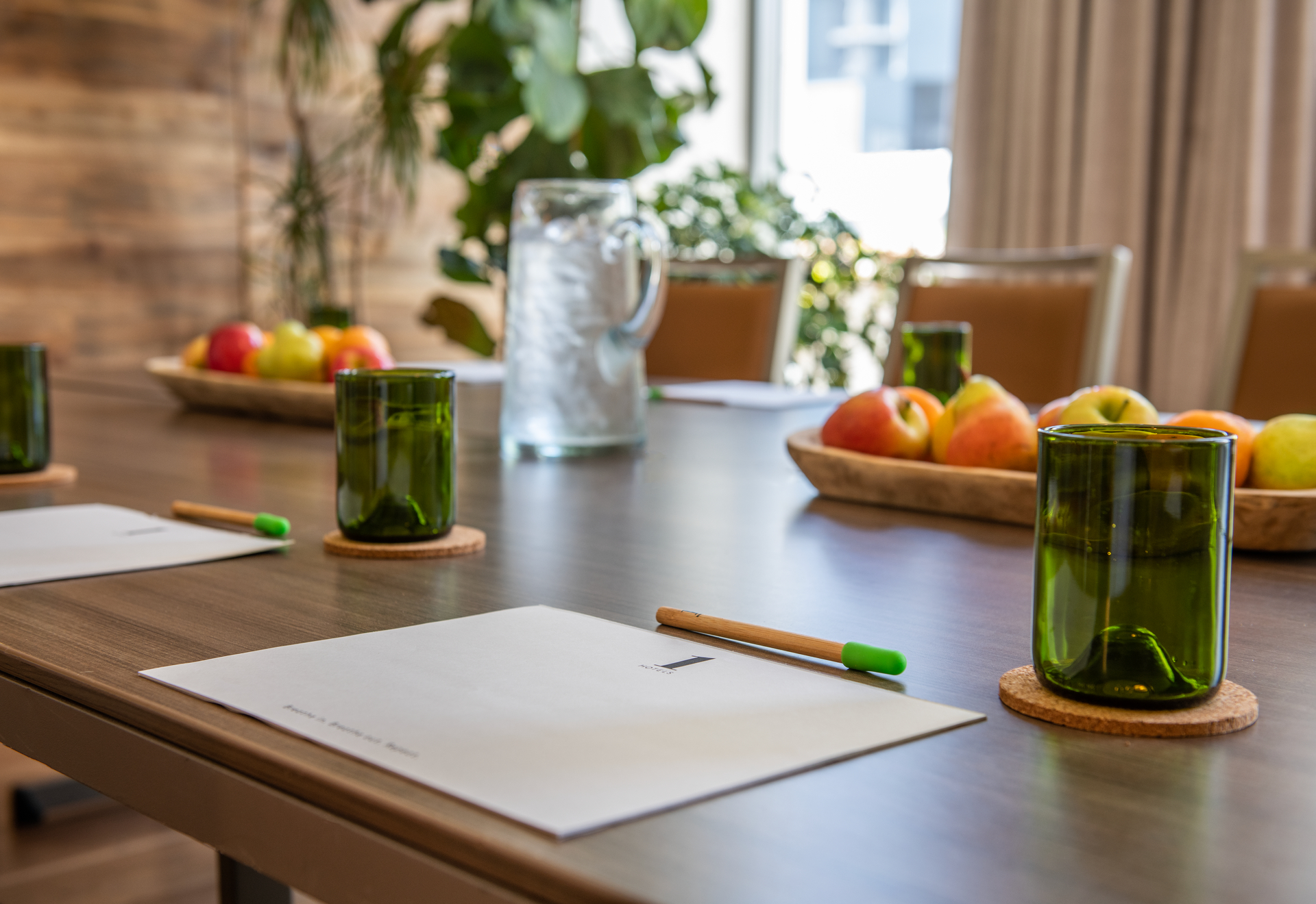 Een houten gedekte tafel met fruit, drinkbekers en papier met potlood per zitplaats