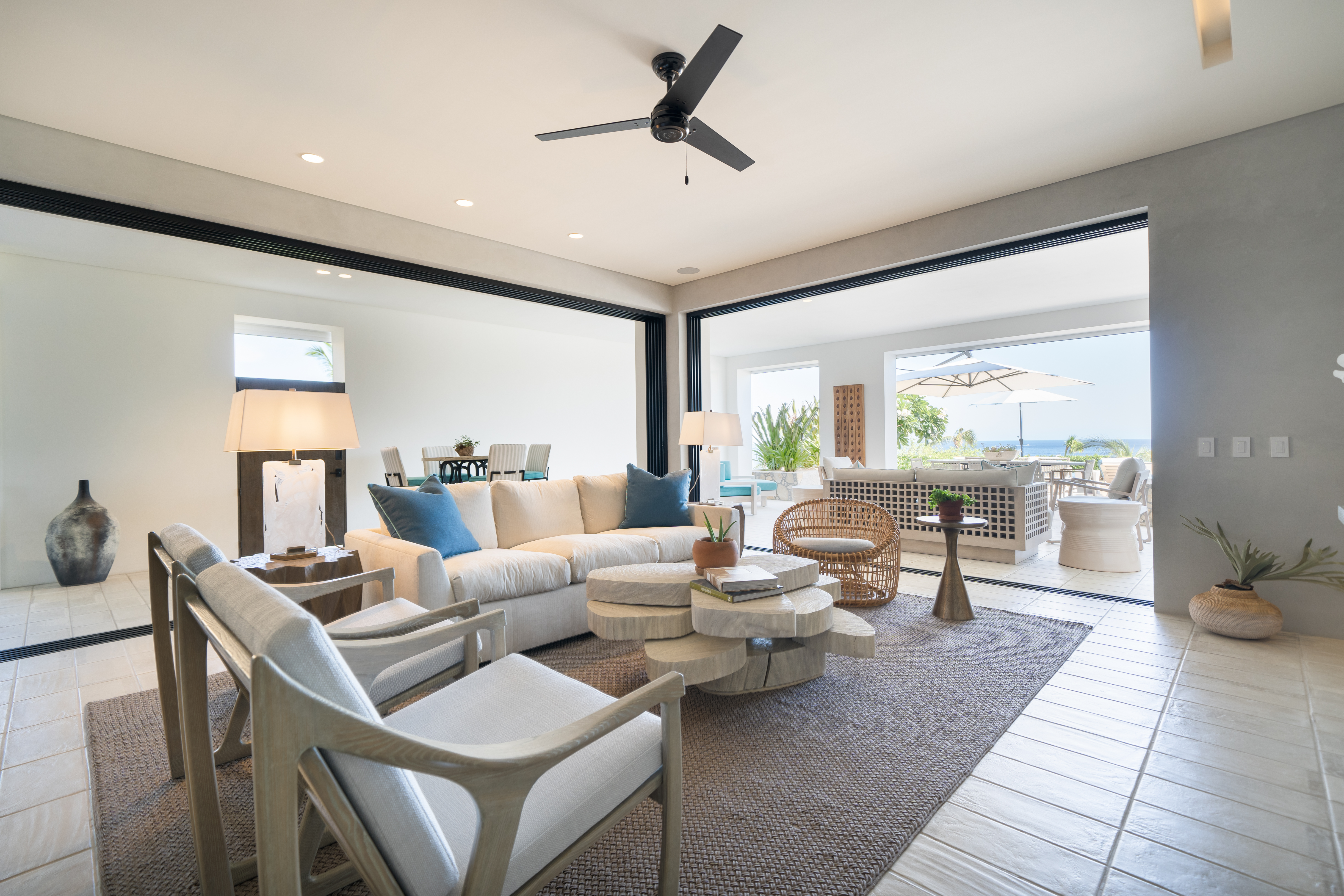 A large furnished room opens onto an outdoor patio with views of the ocean